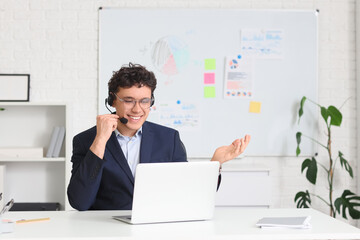 Naklejka premium Young male online business consultant with headset and laptop working in office