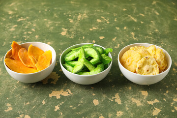 Bowls of different dehydrated fruits on green background