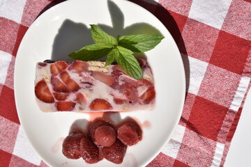 Panna cotta with agar agar decorated by mint leaf and strawberry jam on white plate on red checkered tablecloth, top view © Gulnaz