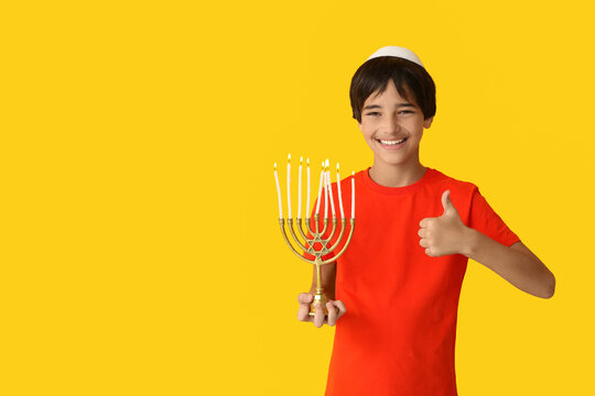 Little Israeli boy in kipa with menorah showing thumb-up gesture on yellow background