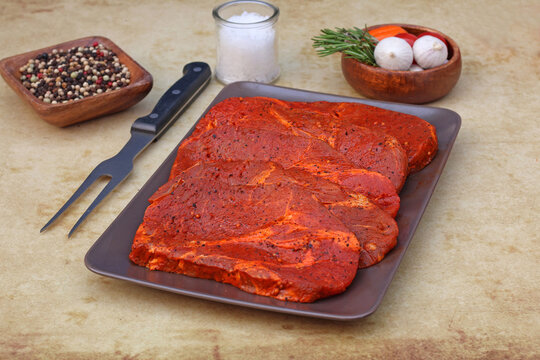 Marinierte Nackensteaks auf Servierplatte mit Fleischgabel und Gew&uuml;rzen.