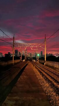 4K footage of public transportation commuter train on railway at dramatic red sunset with city skyline background