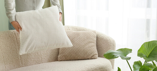woman arranging white cushion on cozy boucle sofa in bright modern living room with soft natural light and green houseplant © Pixel-Shot
