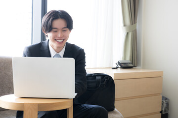 出張先のホテルでノートパソコンを使いオンライン会議などする若いビジネスマン © kapinon