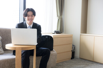 出張先のホテルでノートパソコンを使いオンライン会議などする若いビジネスマン © kapinon