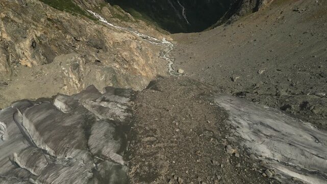 Cinematic aerial drone footage flying above a glacier with blue ice formations, rocky moraine and mountain valley landscape near Odda in western Norway.