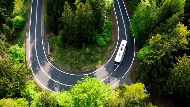 White tourist bus carries passengers along a winding scenic mountain road. Passenger transportation, road trip, bus tour. Aerial view.
