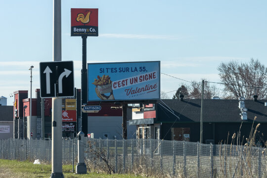 Quebec, Canada, 24 April 2026 : Benny & Co. and Valentine fast food billboards stand alongside a traffic sign on a commercial roadside.