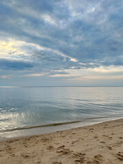 Fototapeta premium Tranquil sandy beach and calm pastel sea under dramatic cloudy sky.