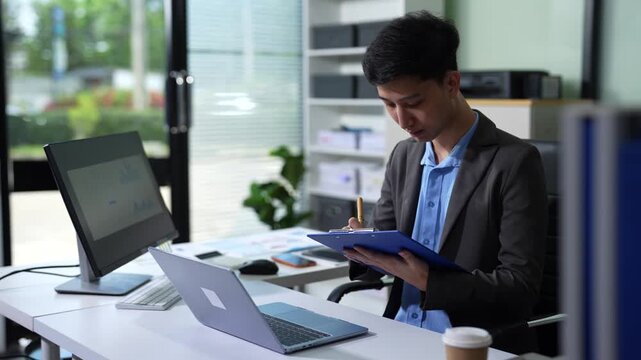 Asian businessman working at office with laptop and documents on table.