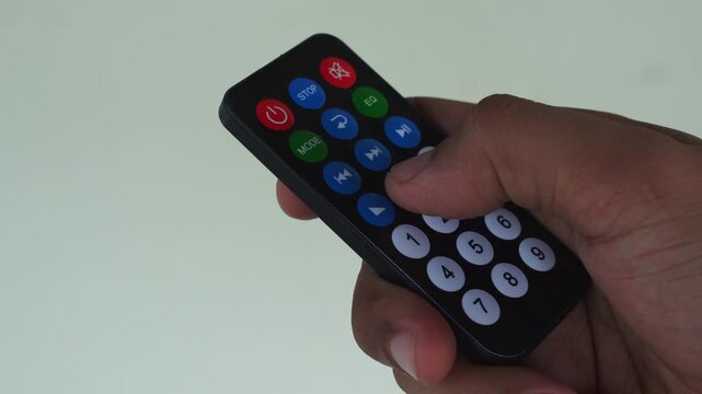 Infrared remote control with colorful buttons being pressed by a human hand, suitable for technology or entertainment concepts.