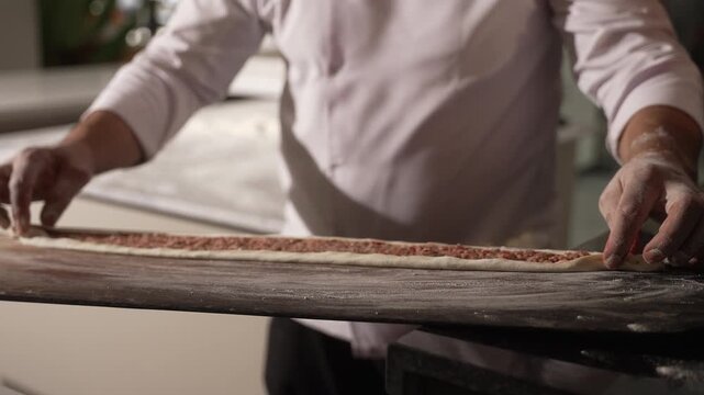 Baker's hands preparing a long dough with minced meat filling, placing it on a wooden peel, fa01