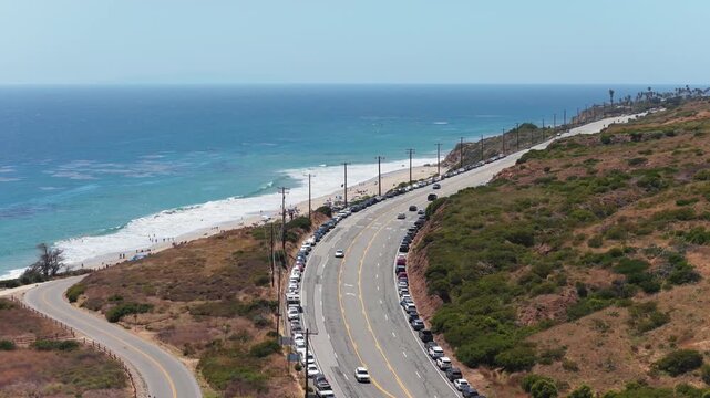 Cars driving on Pacific Coast Highway in Malibu with Santa Monica mountains, expensive real estate properties visible along California coastline