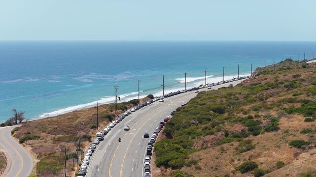 Scenic aerial of Pacific Coast Highway in Malibu with cars driving along picturesque coastline, ocean waves gently crashing on sandy beach