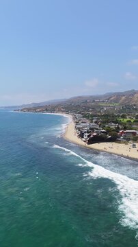 Sunny Malibu California coast showing beachfront real estate properties and sandy Zuma Beach with gentle Pacific Ocean waves on clear day, high angle scenic landmark