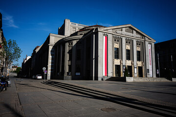 Fototapeta premium City theater building in Katowice Poland with neoclassical facade visitors on steps and quiet urban square under a deep blue sky