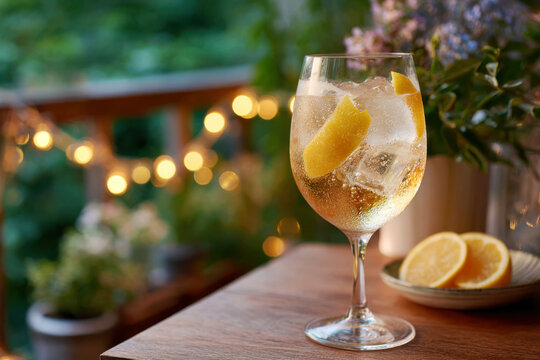 Limoncello spritz with ice and lemon peel in a wineglass on a wooden balcony with string lights at dusk