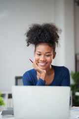 Young smiling African American woman with pencil in hand watching content on laptop, studying...