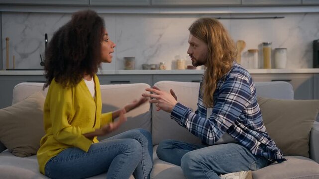 Multiracial couple in conflict at home on couch Caucasian man African woman angry arguing discussing insurance mortgage problem quarrel betrayal jealousy relationship fight domestic violence indoors