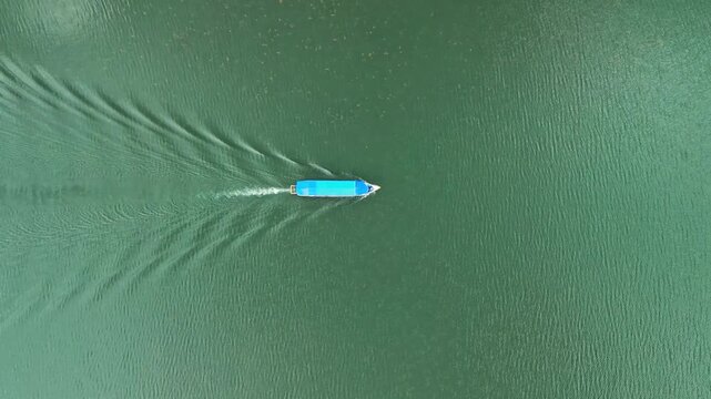 Albania, Shiroka 03 09 2025: Top down symmetrical drone video following a centered boat on Lake Shkodra, capturing the triangular wake trail carved into the calm water surface.
