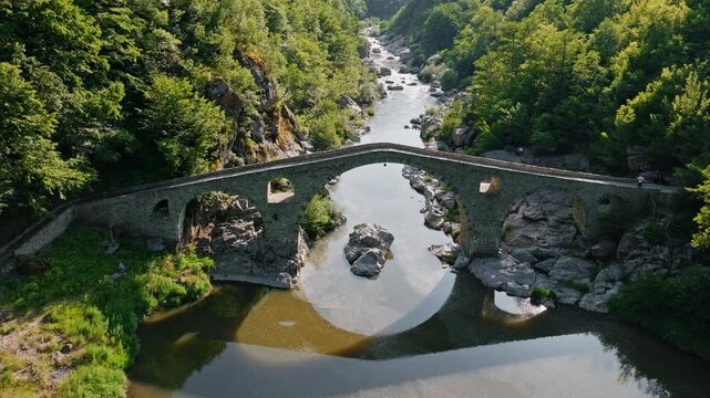 Devil bridge Arda river canyon ancient stone arch structure green forest mountains landscape shadow reflection water surface aerial drone view travel Bulgaria