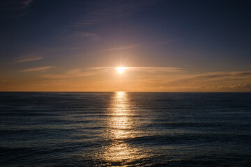 Obraz premium Beautiful golden sunset over the calm sea horizon with sun reflecting on water.