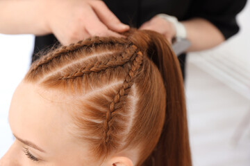Fototapeta premium Hairstylist braiding teenage girl's hair in salon, selective focus