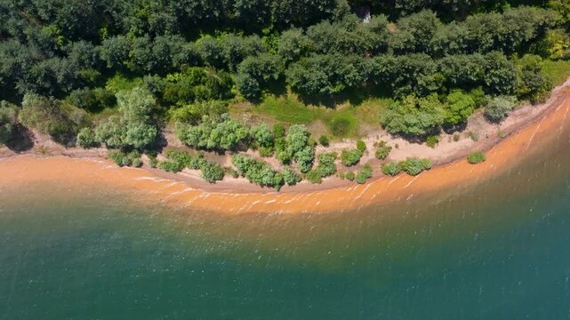 Top down abstract texture lake shore line reddish sand orange soil green bushes pine forest emerald water ripple pattern aerial drone view Shiroka Polyana Bulgaria