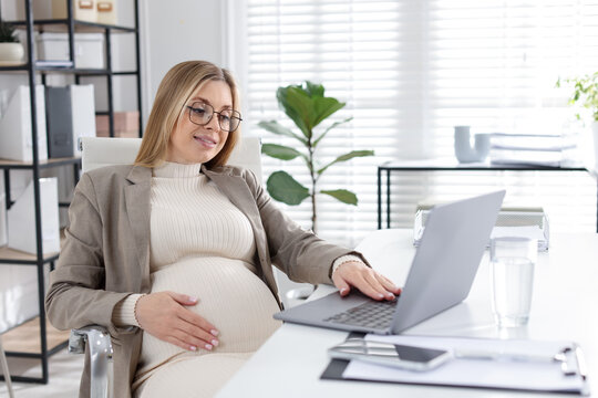Pregnant woman working with laptop at table indoors