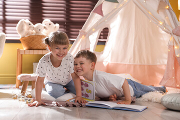 Little girl and boy reading books near wigwam at home © New Africa