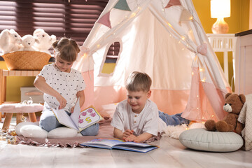 Little girl and boy reading books near wigwam at home © New Africa