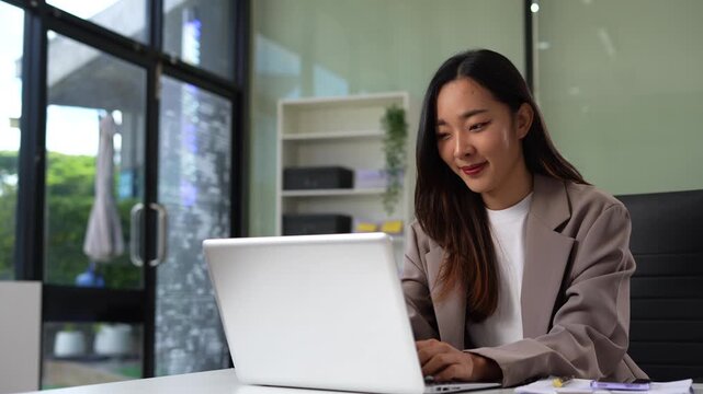 Business woman using computer working online, doing searching, taking notes looking at smartphone at work.