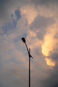 Silhouette of a streetlight against a dramatic sunset sky with clouds.