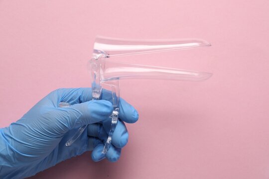 Gynecology tool. Doctor with vaginal speculum on pink background, above view