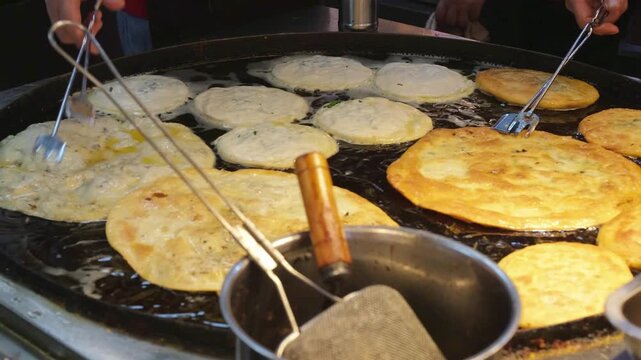 Chef flipping Cong You Bing scallion pancakes on large griddle at Shanghai street food market. Traditional Chinese flatbread preparation and hawker center cooking technique for local culinary culture