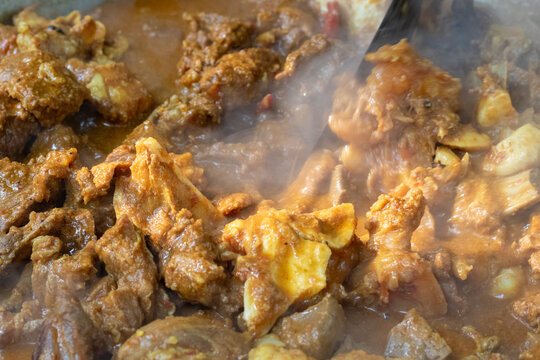Closeup of a flavorful mutton curry cooking in a large metal pot