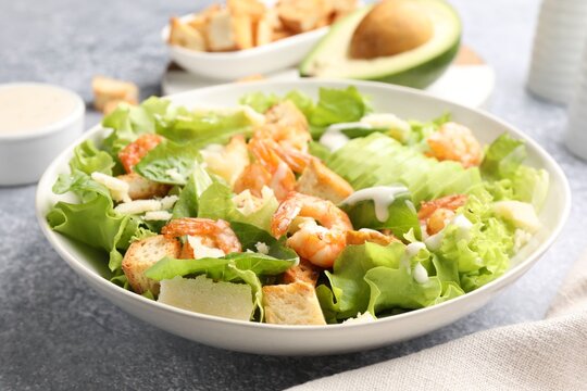 Appetizing Caesar salad with shrimps and avocado served on grey table, closeup