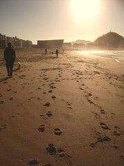 Naklejka premium Gente paseando en la arena de la playa de la Zurriola Donostia San Sebastian con el sol de frente