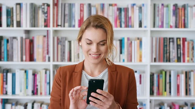 Professor, typing and happy woman with phone in library for academic study, knowledge or information. Female person, teacher or scrolling with smile on smartphone for online curriculum or syllabus
