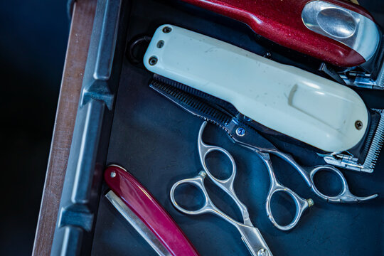 Top view of professional barber tools with clippers, scissors, and razor in a tray.