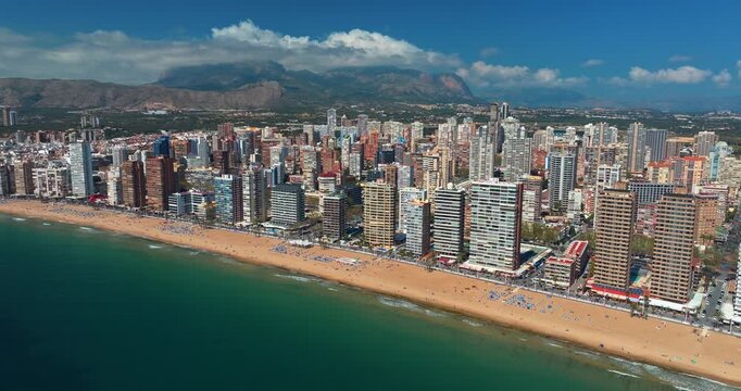 Benidorm aerial panorama sandy beach skyscrapers Mediterranean coastline Spain Alicante summer drone view turquoise sea mountain backdrop resort city skyline slow motion travel