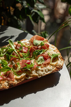 Crispy roman style pizza topped with prosciutto arugula cheese and fresh greens