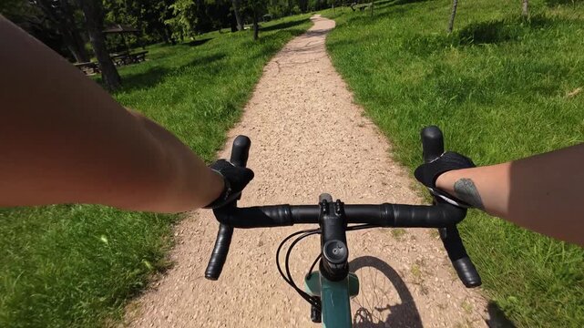 First person view of a cyclist riding a gravel bicycle along a winding trail through a green park. Active outdoor recreation and healthy lifestyle concept with immersive cycling perspective