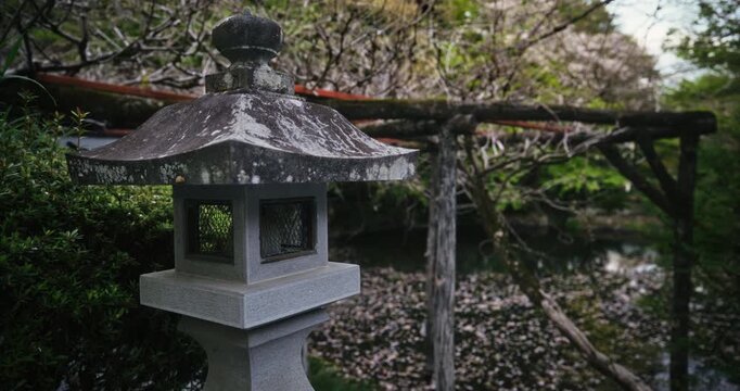 Slow motion shot moving behind ancient, stone Japanese lantern in park