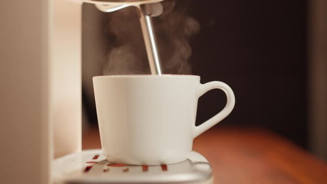 A close-up image of a coffee maker spraying hot water, creating a white brew of coffee. The scene is in slow motion, with steam rising and catching the morning sunlight.