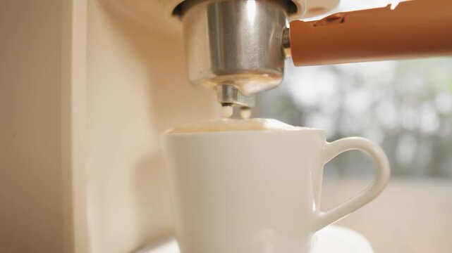 A close-up shot shows a coffee maker pouring hot coffee into a white coffee mug until it's full, with a soft, aromatic foam that's inviting to drink, in the warm morning light. The camera moves smooth