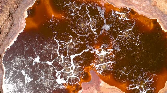 An aerial view of bubbling hot springs in Dallol, Ethiopia, featuring vivid red volcanic terrain and acidic waters