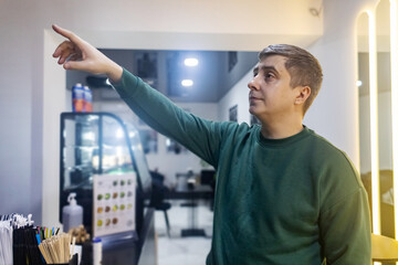 A man looks at desserts in a bakery display case and points to order. Caucasian guy choosing sweets in a cozy cafe counter. © Siniehina