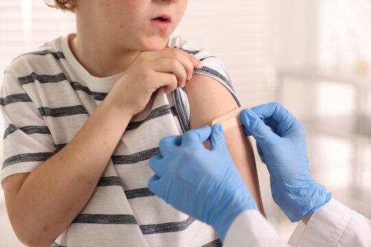 Nurse in medical gloves applying adhesive bandage onto patient's arm after vaccination indoors, closeup