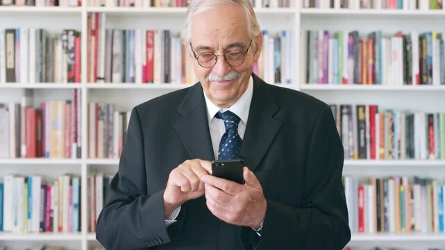 Professor, typing and happy man with phone in library for academic study, knowledge or information. Male person, mature teacher or scrolling with smile on smartphone for online curriculum or syllabus